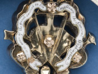 Back side of the gold trophy of a medal with an inscription on a white enamel ribbon